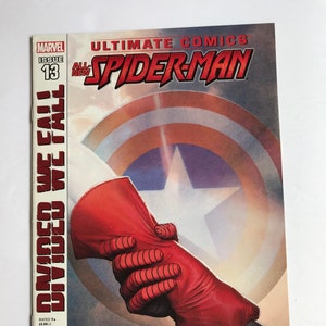 May include: Comic book cover featuring Spider-Man and Captain America shaking hands. The cover is red, white, and blue with the title "Ultimate Comics All-New Spider-Man" and the issue number "13". The tagline is "Divided We Fall".