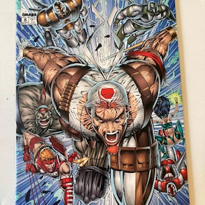 Może przedstawiać: Komiks Youngblood numer 8 z dynamiczną ilustracją na okładce przedstawiającą wiele postaci w pozach akcji. Centralna postać ma białe nakrycie głowy, brązowy ekwipunek i intensywny wyraz twarzy. Tło stanowi niebieskie pole energetyczne.
