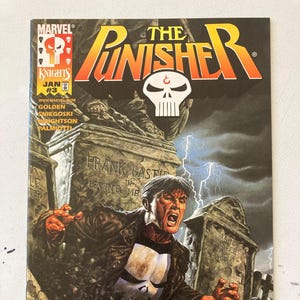 May include: The Punisher comic book cover features a red and yellow title with the word "Punisher" in large letters. The cover art depicts a man in a black leather jacket and skull mask standing in a graveyard. The text on the cover reads "Frank Castle Loving Me" and "Wrightson Qosko 98".