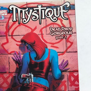 May include: Comic book cover featuring Mystique, a blue-skinned superhero, in a red tank top and black pants. The cover is titled "Mystique: Dead Drop Gorgeous Part 5".