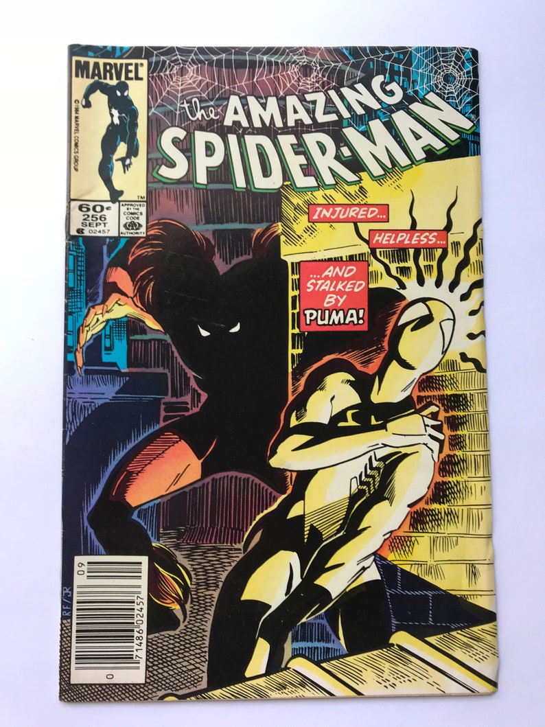 May include: A vintage Marvel comic book titled The Amazing Spider-Man issue 256 from September 1984. The cover features a black silhouette of a character stalking a white-clad figure with the text Injured... Helpless... And Stalked By Puma!