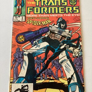 May include: Comic book cover for The Transformers #3, featuring a dynamic illustration of Transformers and Spider-Man. The cover is predominantly orange, with text and images in blue, black, and white. The Marvel logo is visible in the upper left corner.