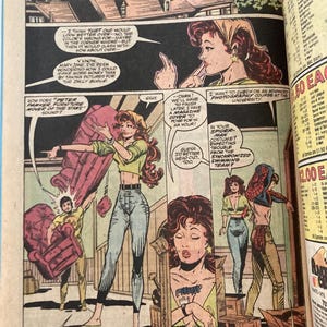 Pu&ograve; includere: Pagina di fumetto con una donna in top verde e jeans, che sposta un divano rosso con un uomo. Le nuvolette contengono dialoghi. La striscia di fumetti &egrave; a colori e ha uno stile vintage.