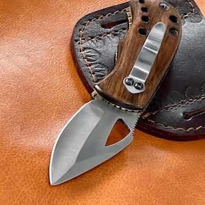 May include: A brown wooden handled pocket knife with a silver blade and a leather sheath. The knife has a unique design with a hole in the blade.