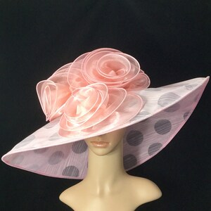 May include: A pink and white polka dot hat with a large pink flower on top. The hat is made of a soft, sheer fabric.