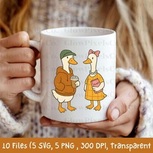 K&ouml;nnte beinhalten: Wei&szlig;e Keramiktasse mit einer Cartoon-Illustration von zwei G&auml;nsen. Eine Gans tr&auml;gt einen braunen Kapuzenpullover und h&auml;lt einen Kaffeebecher, die andere ein gelbes Kleid und ein Buch mit der Aufschrift "PLANS". Die Tasse hat eine gl&auml;nzende Oberfl&auml;che.