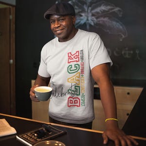 Peut inclure: Un t-shirt gris clair avec le mot "BLACK" en texte vertical rouge, vert et jaune. Le t-shirt présente également les mots "Celebrate" et "History, Culture, Excellence, Respect" dans un design vertical.