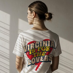 May include: Cream-colored t-shirt with the text "VIRGINIA IS FOR THE LOVERS" in a retro design. The text is set against a red heart shape with yellow and blue accents. The shirt is short-sleeved.