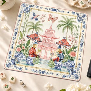 Peut inclure: Un tapis de mah-jong carré orné d'une illustration centrale de deux singes assis sous des parasols rouges à motifs près d'une pagode rose, entourés de palmiers, de fleurs et de papillons, encadrés par une bordure en bambou floral bleu et blanc.