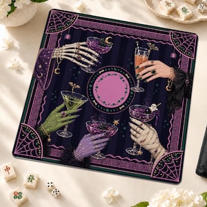 May include: A square mat featuring a dark purple and black striped background with a central pink circle. Four hands, including a skeleton hand, a green hand, a purple hand, and a bandaged hand, hold cocktail glasses. The border has spiderwebs.