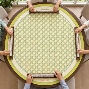 May include: A round mahjong table mat with a cream and light green woven pattern, featuring dark wood tile racks on four sides. The mat includes printed text labels reading WALLS LEFT and PLAY RIGHT in a circular border around the game area.