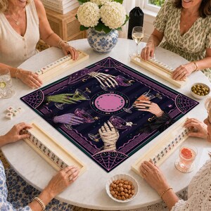 May include: A square game mat featuring a dark purple and black striped background with a central pink circle. The design displays four hands, including skeletal, green, purple, and mummy-wrapped versions, each holding a cocktail glass.