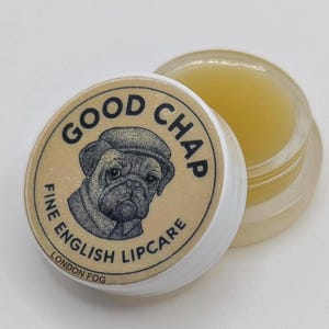 May include: A small, clear lip balm pot with a white lid. The lid has a pug illustration and the text "GOOD CHAP FINE ENGLISH LIPCARE LONDON FOG". The lip balm inside is a pale yellow colour.