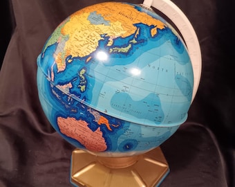May include: A vintage globe with a blue ocean and tan landmasses. The globe has a white meridian ring with degree markings and sits on a gold-colored hexagonal base. The globe is a decorative educational tool.
