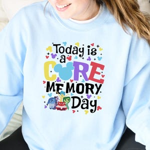 May include: Pale blue crew neck sweatshirt with the phrase "Today is a CORE MEMORY Day" in vibrant colours and Disney character graphics. The sweatshirt has a relaxed fit and long sleeves, suitable for everyday wear.