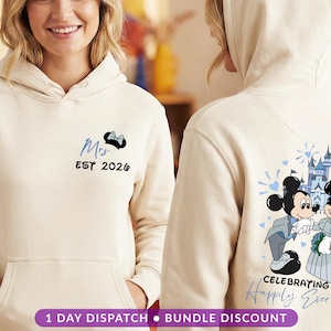 May include: Cream-coloured hoodie with a front pocket and a hood. The front features the word "Mrs" in blue script, a black bow, and the year "2026". The back displays a cartoon of Mickey and Minnie Mouse in wedding attire, with a castle.