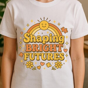 Puede incluir: Camiseta blanca con un diseño retro que presenta un sol sonriente, un arcoíris y el texto "Shaping Bright Futures" en naranja y amarillo. El diseño incluye estrellas, flores, corazones y piezas de rompecabezas.