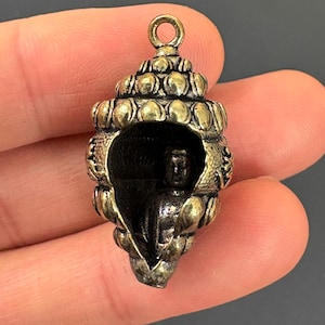 Peut inclure: Un pendentif détaillé de couleur bronze en forme de coquillage, avec une petite figurine à l'intérieur. Le pendentif a une boucle en haut pour l'accrocher et des détails complexes à l'extérieur. Le design général est orné et décoratif.