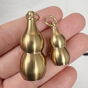 May include: Two small, gold-colored gourd-shaped pendants. Each pendant has a loop at the top for attaching to a chain or other item. The pendants are made of a shiny, metallic material.