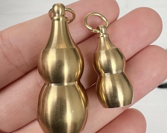 May include: Two small, gold-colored gourd-shaped pendants. Each pendant has a loop at the top for attaching to a chain or other item. The pendants are made of a shiny, metallic material.
