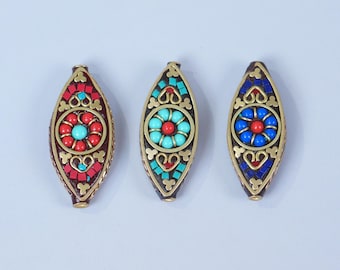 Könnte beinhalten: Drei dekorative ovale Anhänger mit aufwendigen Designs. Jeder Anhänger hat ein zentrales Blumenmuster mit roten, türkisfarbenen oder blauen Perlen, umgeben von einem goldfarbenen Metallrahmen und farbigen Mosaikakzenten. Die Anhänger werden vor einem hellen Hintergrund gezeigt.