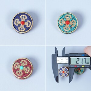 K&ouml;nnte beinhalten: Drei runde, dekorative Objekte mit aufwendigen Designs. Jedes St&uuml;ck hat einen zentralen Edelstein und ein Mosaik aus farbigen Steinen, eingebettet in einen goldfarbenen Metallrahmen. Das digitale Messschieber zeigt eine Messung von 21,7 mm.