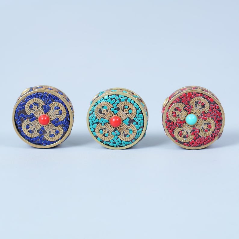 K&ouml;nnte beinhalten: Drei runde, dekorative Boxen mit aufwendigen Mosaikdesigns. Eine ist blau mit roter Mitte, eine weitere t&uuml;rkis mit roter Mitte und die dritte rot mit t&uuml;rkiser Mitte. Jede hat ein goldfarbenes Metallband.