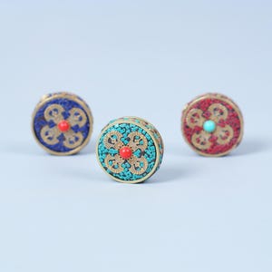K&ouml;nnte beinhalten: Drei dekorative runde Boxen mit Mosaikmustern. Eine ist blau mit roter Mitte, eine andere t&uuml;rkis mit roter Mitte, und die dritte ist rot mit t&uuml;rkiser Mitte. Jede Box hat einen goldfarbenen Metallrand.