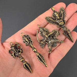 May include: Four antique brass pendants with detailed designs. The pendants depict various figures and shapes, including a bird-like creature, a deity, and a stylized leaf. Each pendant has a loop for hanging.