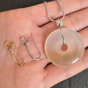 May include: A silver necklace with a circular, light-coloured pendant and two pairs of earrings. One pair is gold-coloured, and the other is silver. The pendant has a hole in the centre.