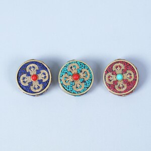 K&ouml;nnte beinhalten: Drei runde, dekorative Ornamente mit aufwendigen Designs. Jedes hat einen goldfarbenen Rand und ein zentrales Blumenmuster. Eines ist blau mit roter Mitte, ein anderes t&uuml;rkis mit roter Mitte, und das dritte ist rot mit t&uuml;rkiser Mitte.