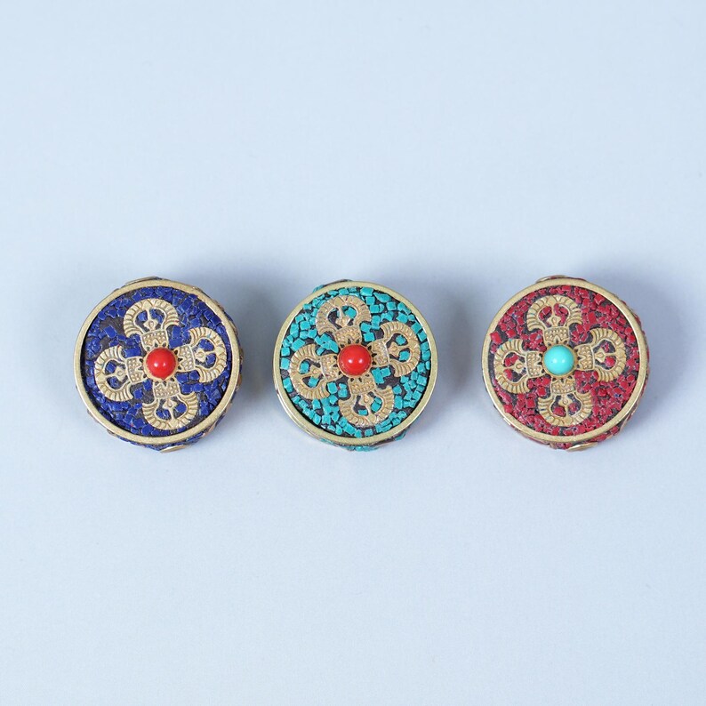 K&ouml;nnte beinhalten: Drei runde, dekorative Ornamente mit aufwendigen Designs. Jedes hat einen goldfarbenen Rand und ein zentrales Blumenmuster. Eines ist blau mit roter Mitte, ein anderes t&uuml;rkis mit roter Mitte, und das dritte ist rot mit t&uuml;rkiser Mitte.