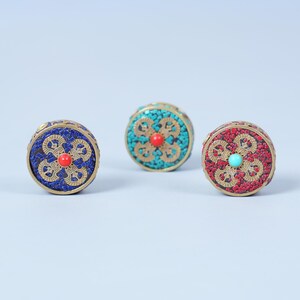 K&ouml;nnte beinhalten: Drei kleine, runde dekorative Boxen mit aufwendigen Designs. Eine ist blau mit roter Mitte, eine andere t&uuml;rkis mit roter Mitte und die dritte rot mit t&uuml;rkiser Mitte. Jede hat ein goldfarbenes Metallband.