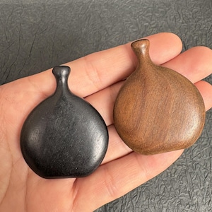 May include: Two small, smooth, teardrop-shaped wooden objects with narrow necks. One object is a deep, solid black colour with a visible wood grain, while the other is a warm, medium-brown colour with a prominent, natural wood grain pattern.