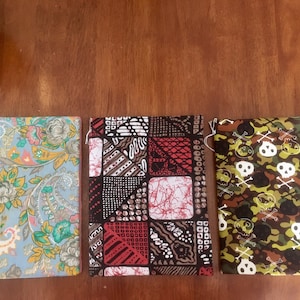May include: Three fabric pouches with different patterns. The first pouch is light blue with a floral pattern. The second pouch is black with a red, white, and brown geometric pattern. The third pouch is green and brown camouflage with white skull and crossbones.