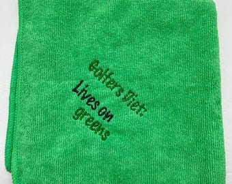 May include: Green microfiber cleaning cloth with the embroidered text "Golfers Diet: Lives on greens".