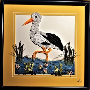 May include: A white and black paper quilled stork standing in a blue water scene with green reeds. The artwork is framed in a yellow and black frame.
