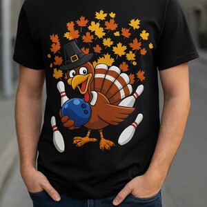 May include: Black t-shirt featuring a cartoon turkey wearing a pilgrim hat and holding a blue bowling ball. The turkey is surrounded by bowling pins and autumn leaves. A fun design for Thanksgiving or bowling enthusiasts.