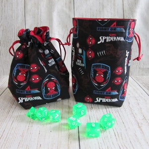 May include: Two black drawstring bags with a red lining and a Spider-Man print. The bags are filled with green dice. The bags have the text "Fight On Spider-Man" and "Spider Sense" printed on them.
