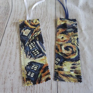 May include: Two fabric bookmarks with a yellow and blue Starry Night design. One bookmark has a white ribbon and the other has a blue ribbon.