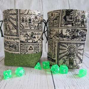 May include: Two green fabric dice bags with a white and black print of a video game character. The bags have a drawstring closure. Green dice are scattered in front of the bags.