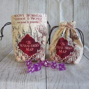 May include: Two beige fabric drawstring bags with the Marauder's Map design from the Harry Potter series. The bags are filled with purple dice. The text on the bags reads "Moony, Wormtail, Padfoot & Prongs are proud to present The Marauder's Map".