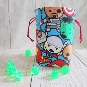 May include: A red drawstring bag with a blue background and a pattern of cartoon superheroes. The bag is filled with green dice.