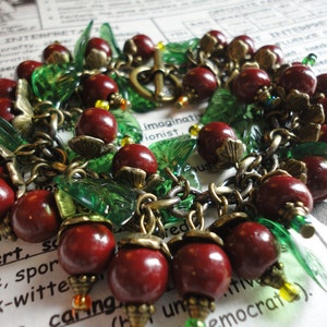 May include: A red and green charm bracelet with leaves, beads, and metal charms. The bracelet is made of metal and has a chain link design.