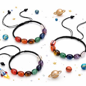 May include: Three black cord bracelets with colorful gemstone beads. Each bracelet features a different arrangement of red, orange, brown, green, blue, purple, and pink beads. Decorative space-themed elements like planets and stars surround the bracelets.