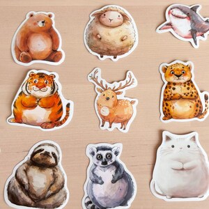 K&ouml;nnte beinhalten: Eine Sammlung von Aquarell-Tieraufklebern, darunter ein Schwein, ein B&auml;r, ein Schaf, ein Hai, eine Robbe, ein Tiger, ein Hirsch, ein Leopard, ein Koala, ein Panda, ein Faultier, ein Lemur, eine Katze und ein Kaninchen. Jeder Aufkleber hat einen wei&szlig;en Rand.