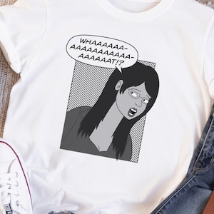 May include: White t-shirt with a black and white cartoon graphic of a woman with glasses and long hair, exclaiming "WHAAAAAAA-AAAAAAAAAAAAAAT!?" The shirt is paired with blue jeans, white trainers, and a watch.
