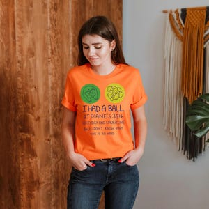 May include: Orange t-shirt with rolled sleeves featuring the text "I HAD A BALL AT DIANE'S 35th BIRTHDAY AND UNDERLINE BALL I DON'T KNOW WHY THIS IS SO HARD". The shirt has two circular graphics.