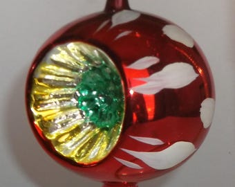 Peut inclure: Une boule de Noël sphérique en verre rouge avec une finition réfléchissante et une indentation circulaire. L'indentation contient un motif floral texturé jaune et vert. La surface extérieure est ornée de formes de feuilles blanches peintes.