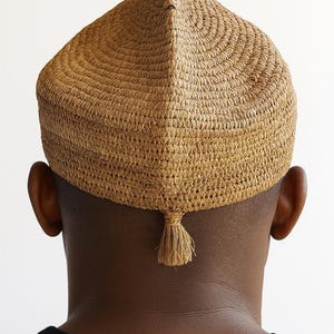 Peut inclure: Un chapeau tissé brun clair avec un sommet pointu et une petite gland à l'arrière. Le chapeau est fait de fibres naturelles et a un aspect texturé. Le chapeau est porté par une personne à la peau foncée et une chemise noire.